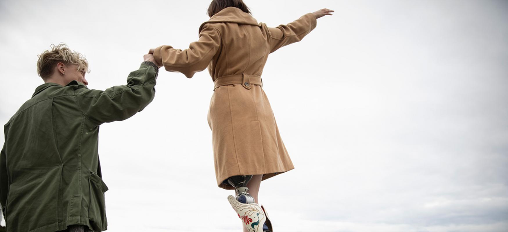 Man holding hands with girl walking by the sea with a prosthetic leg.
