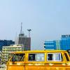 A yellow minivan driving in front of office buildings in Lagos, Nigeria.