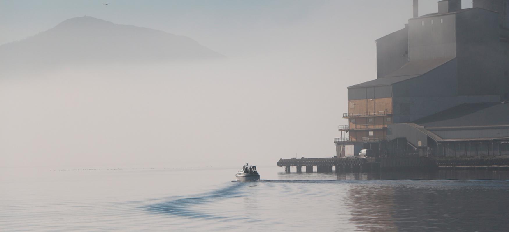 White boat driving slowly past an industrial building.
