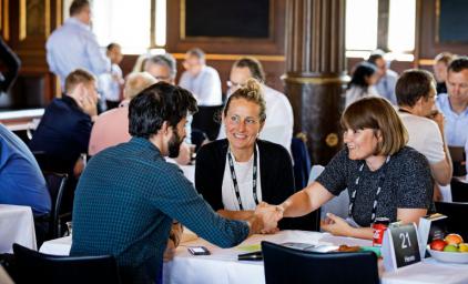 Two persons shaking hands with another person is watching while they all sit around a roundtable at the Nordic Impact Business Summit 2019.