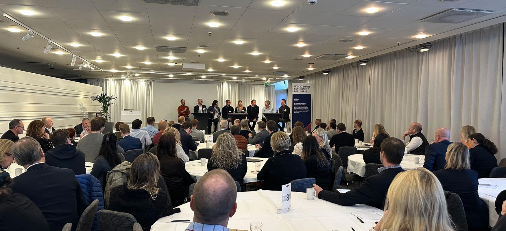 Konference. Personer på en scene og en sal fyldt med mennesker