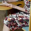 A woman in a flower dress sitting at a cafe table with the text "is this a designer"?