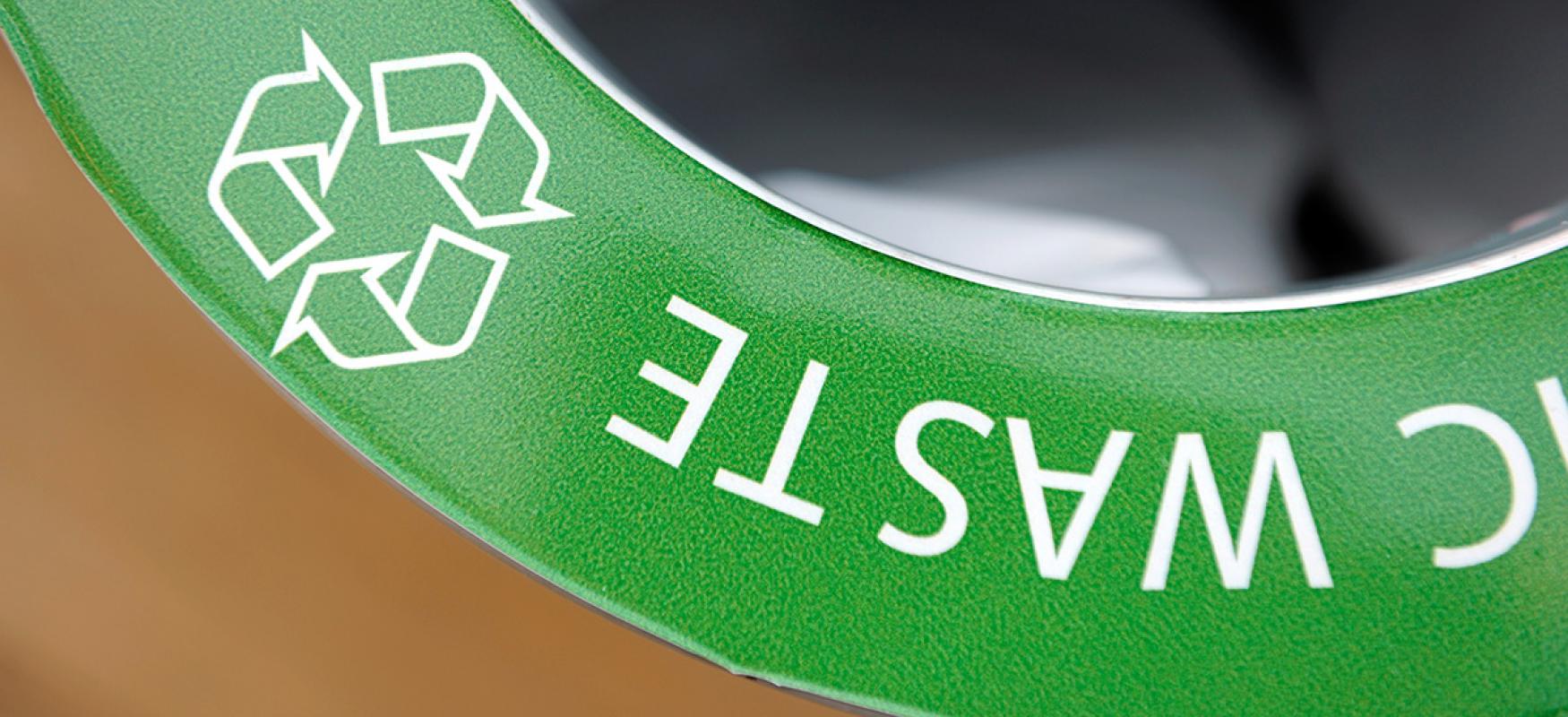 Closup of a green sign saying "Waste" and with a classic recycling logo.