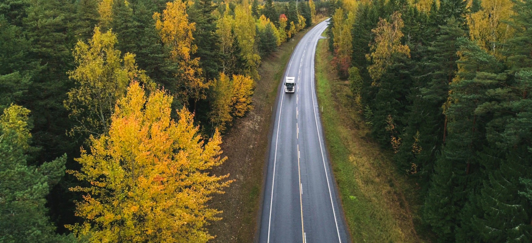 Truck driving on a empty road through a forest in fall colors